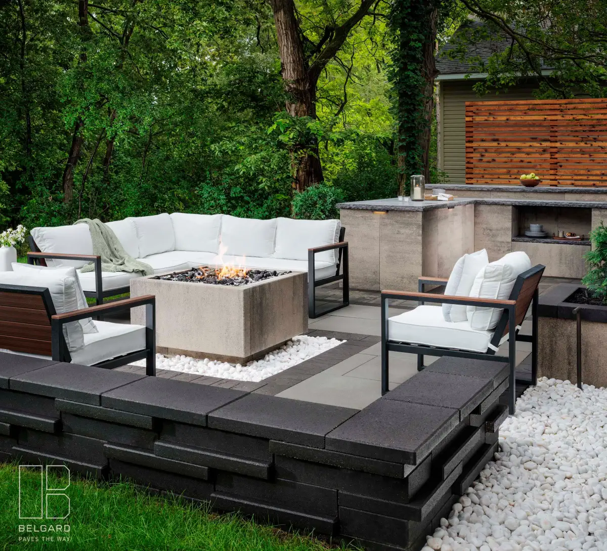 Lounge seating, a square fire feature and an outdoor counter on a paved patio