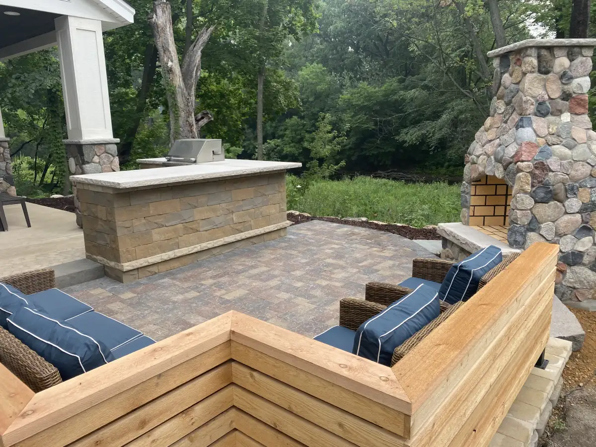 Outdoor kitchen, stone fireplace and built-in wood seating around a paver patio