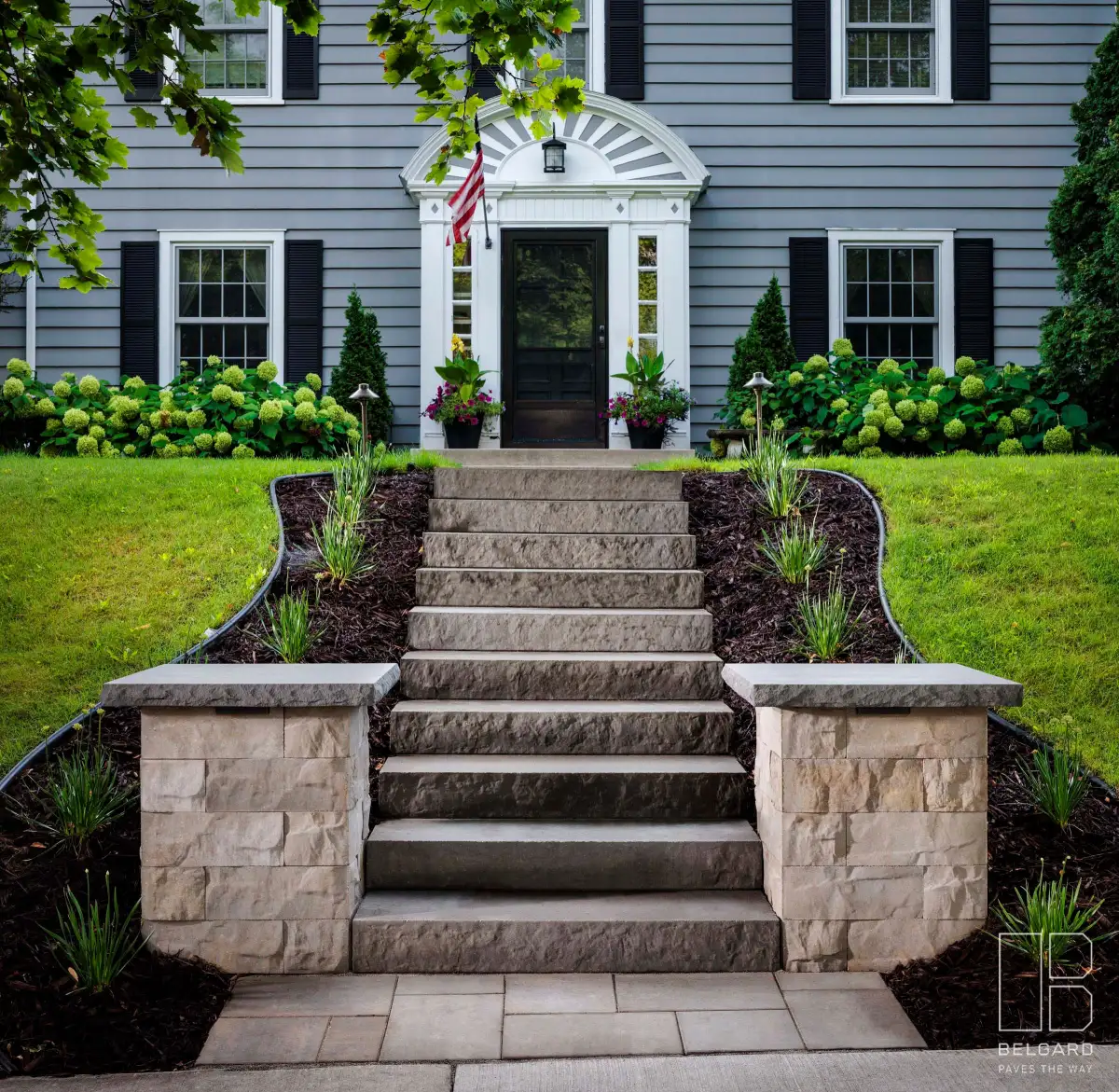 Front entry staircase with stone side walls and planted borders leading to a gray house